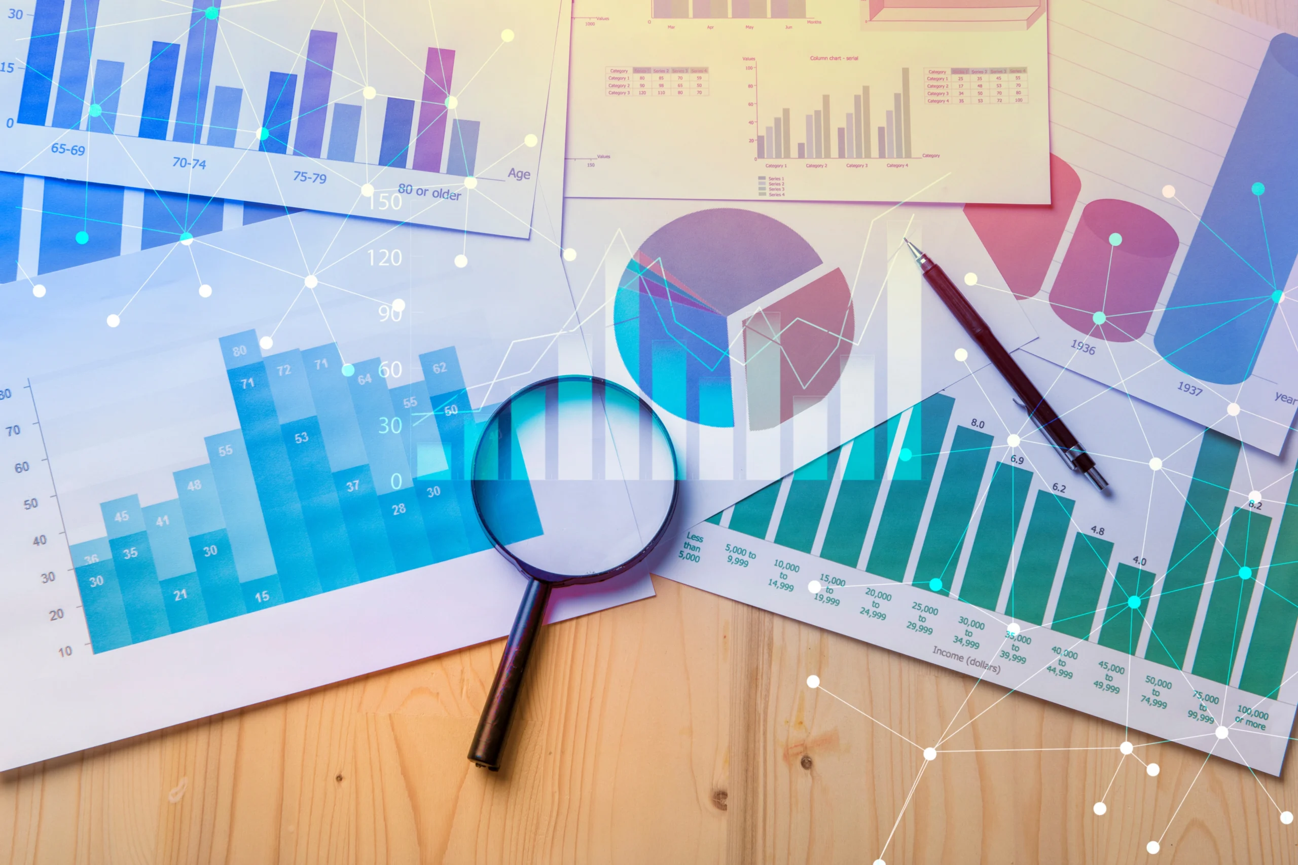 A stock image of a magnifying glass on top of printed charts and graphs