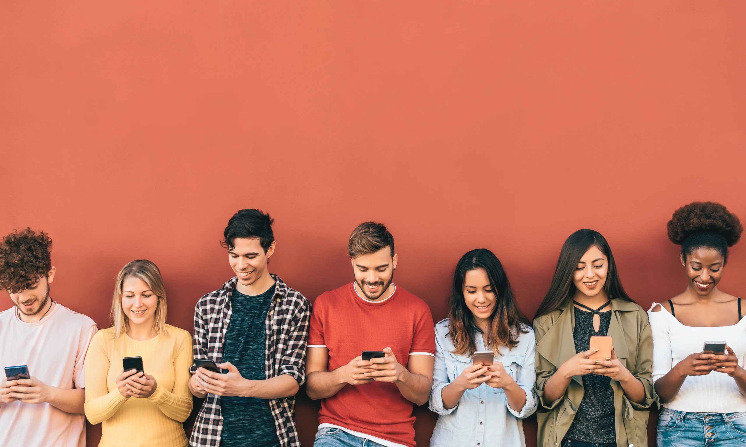 A stock photo of a group of Gen Zers standing together and laughing at their phones