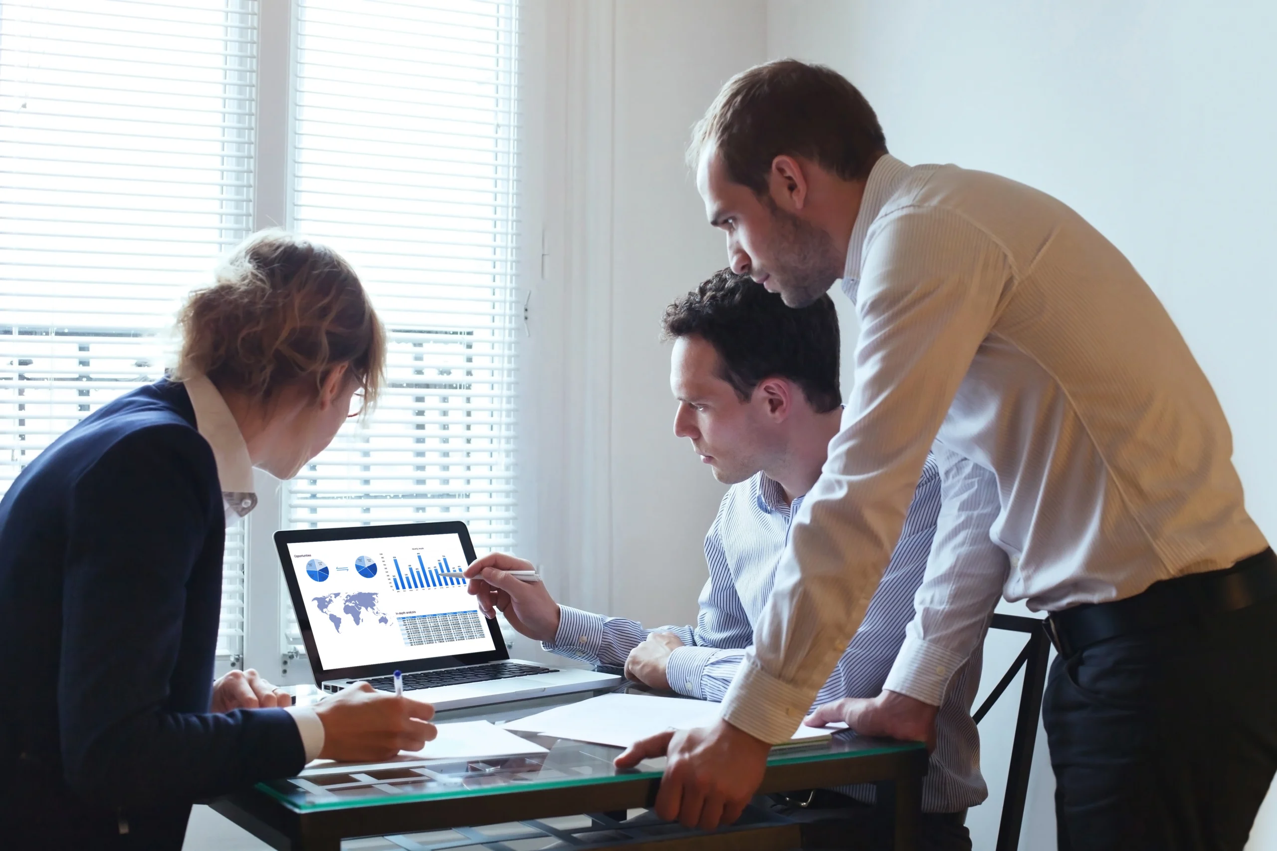 A stock image of a team of three market researchers poring over a computer with charts and graphs on the screen