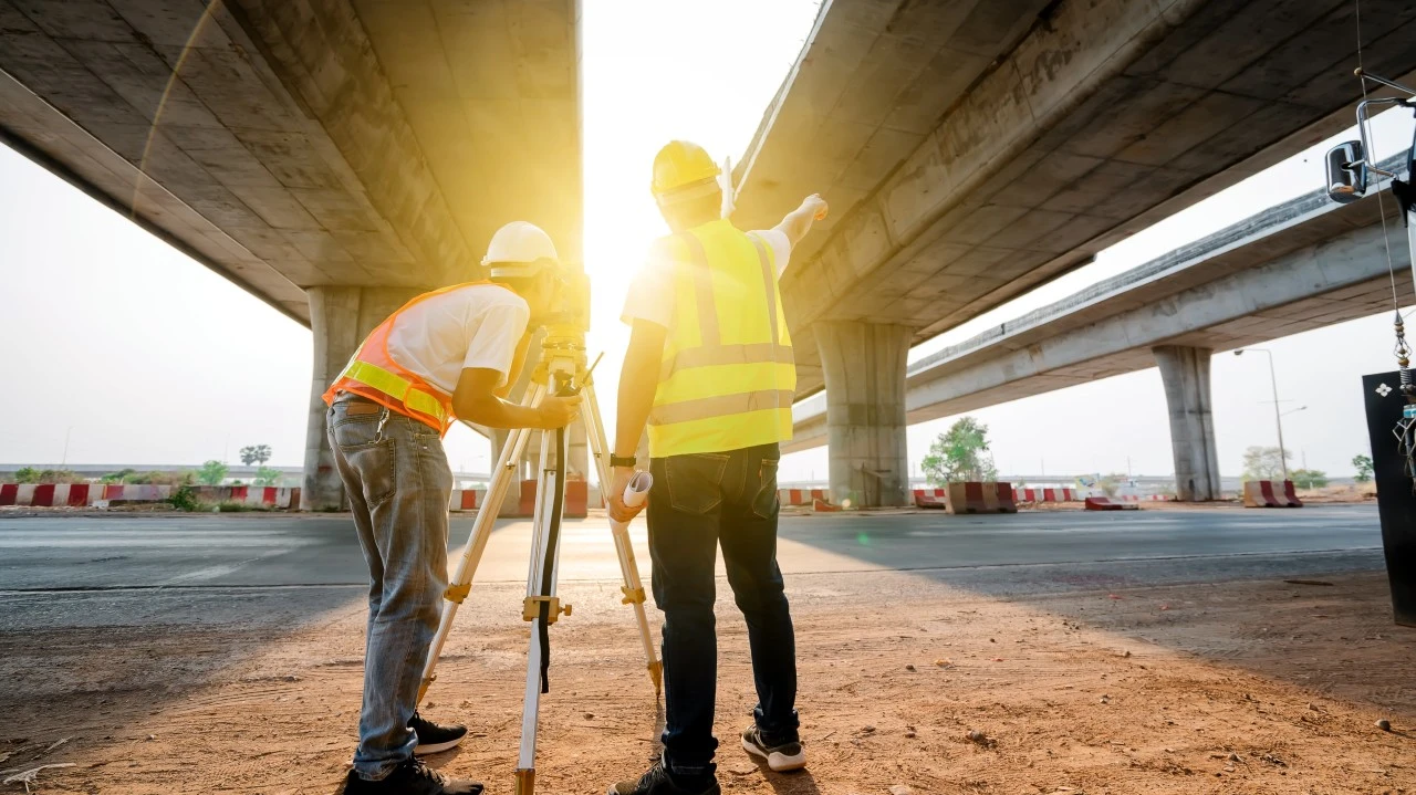 Two surveyors working underneath a bridge at sunset.